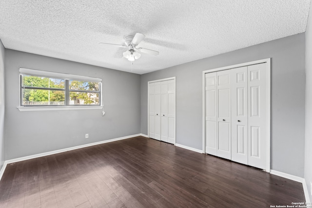 unfurnished bedroom featuring a textured ceiling, ceiling fan, dark wood-type flooring, and multiple closets