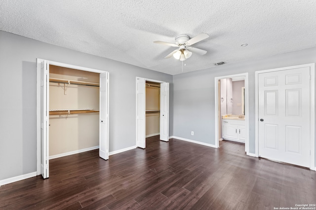 unfurnished bedroom featuring ceiling fan, a textured ceiling, multiple closets, ensuite bath, and dark hardwood / wood-style flooring