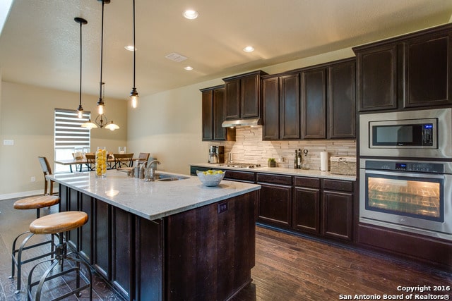 kitchen with hanging light fixtures, dark hardwood / wood-style flooring, stainless steel appliances, a center island with sink, and sink