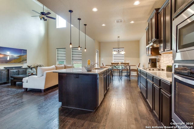 kitchen featuring dark brown cabinets, decorative light fixtures, a kitchen island with sink, dark wood-type flooring, and appliances with stainless steel finishes