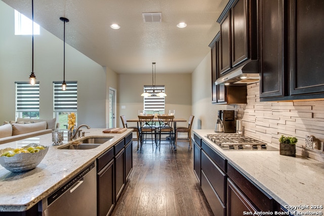 kitchen featuring light stone counters, dark brown cabinetry, decorative light fixtures, stainless steel appliances, and dark hardwood / wood-style floors