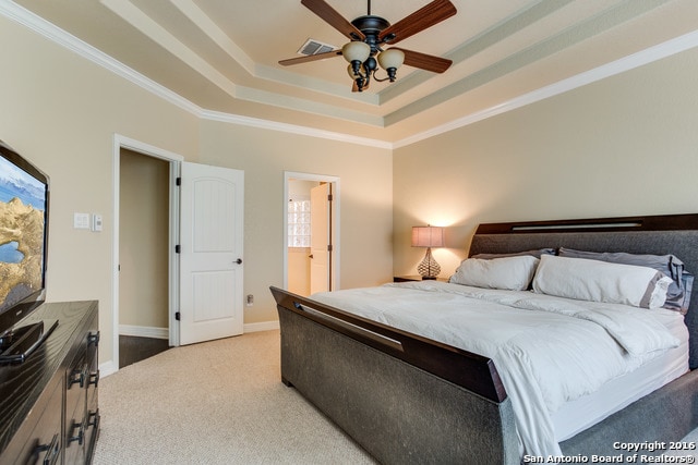 carpeted bedroom with crown molding, ceiling fan, and a raised ceiling