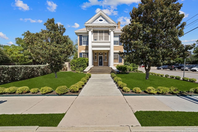 neoclassical home with a balcony and a front lawn