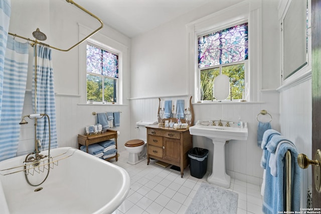 bathroom with tile patterned flooring, a bathtub, a healthy amount of sunlight, and toilet