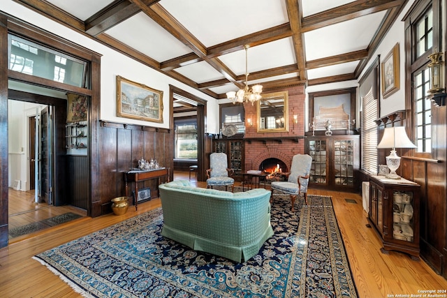 living room featuring light hardwood / wood-style floors, beamed ceiling, coffered ceiling, an inviting chandelier, and a brick fireplace