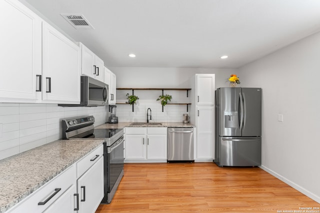 kitchen featuring white cabinets, sink, stainless steel appliances, light wood-type flooring, and decorative backsplash