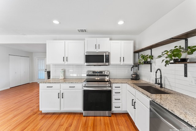 kitchen featuring sink, backsplash, white cabinetry, appliances with stainless steel finishes, and light wood-type flooring