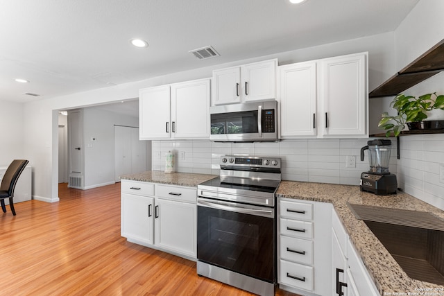 kitchen featuring decorative backsplash, light hardwood / wood-style floors, white cabinetry, light stone counters, and stainless steel appliances