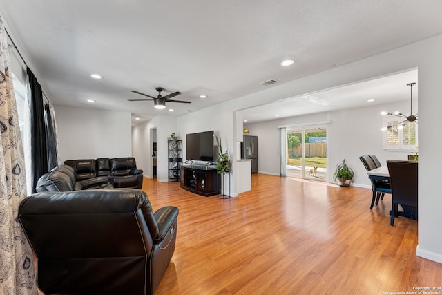 living room featuring ceiling fan with notable chandelier and light wood-type flooring