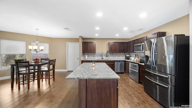 kitchen with dark brown cabinetry, a kitchen island, decorative light fixtures, light hardwood / wood-style flooring, and stainless steel appliances