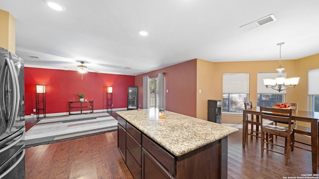 kitchen with pendant lighting, a kitchen island, refrigerator, ceiling fan with notable chandelier, and dark hardwood / wood-style flooring