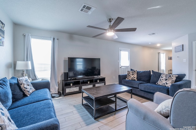 living room featuring light hardwood / wood-style flooring, ceiling fan, and a textured ceiling