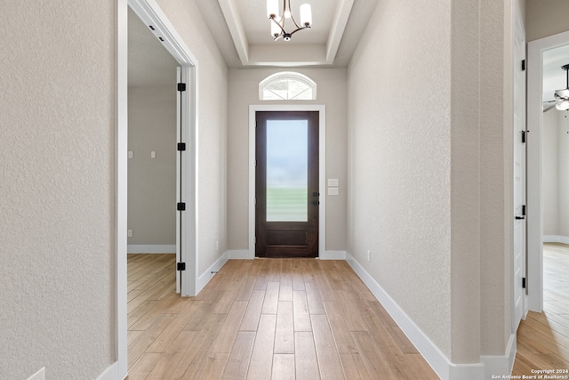 foyer entrance with ceiling fan with notable chandelier, light hardwood / wood-style floors, and a tray ceiling