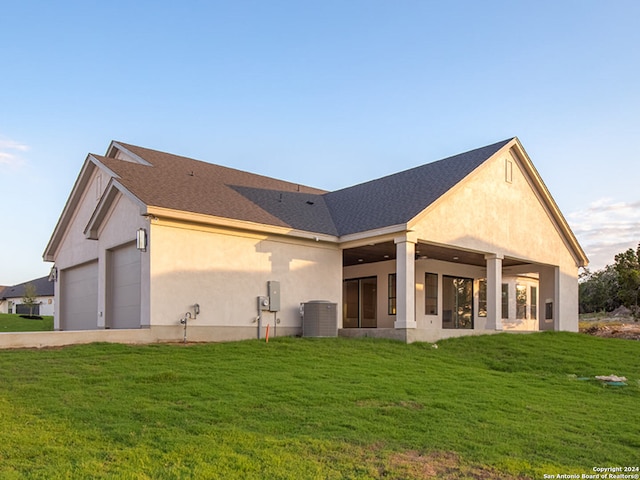 back of property featuring a yard, a garage, and central AC unit