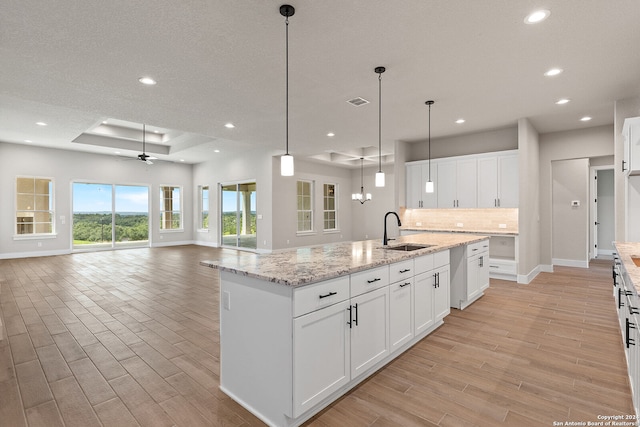 kitchen featuring ceiling fan, sink, light hardwood / wood-style flooring, white cabinets, and an island with sink