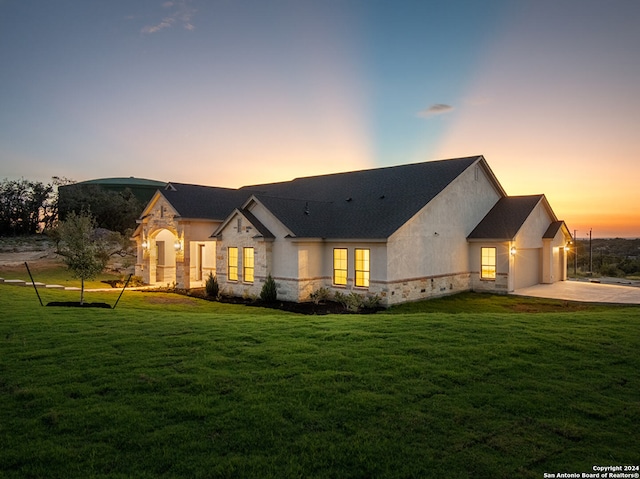 back house at dusk featuring a lawn and a garage