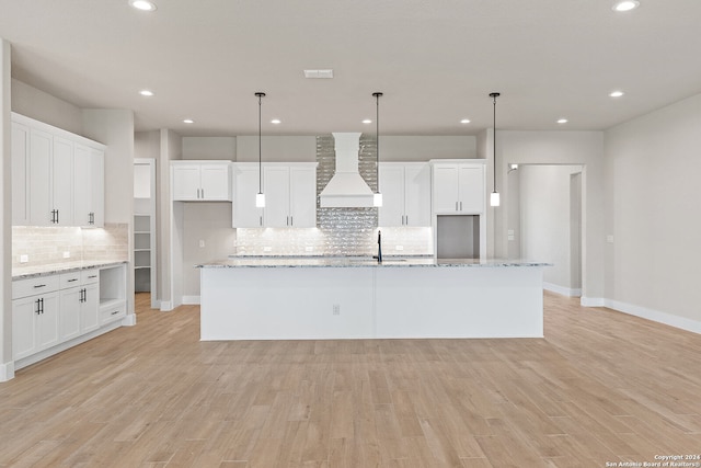 kitchen with premium range hood, a kitchen island with sink, pendant lighting, and light hardwood / wood-style floors