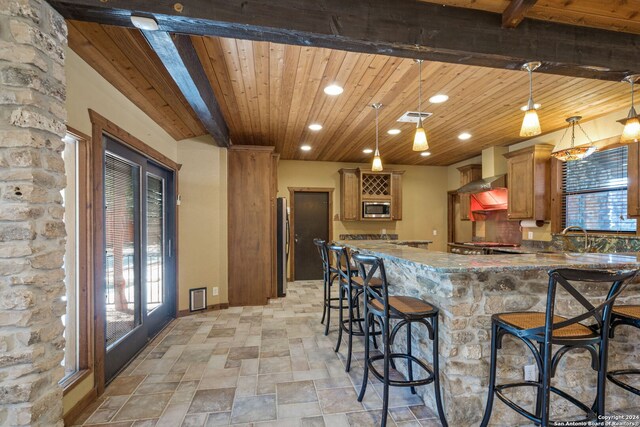 kitchen with beamed ceiling, wood ceiling, decorative light fixtures, stone counters, and stainless steel microwave