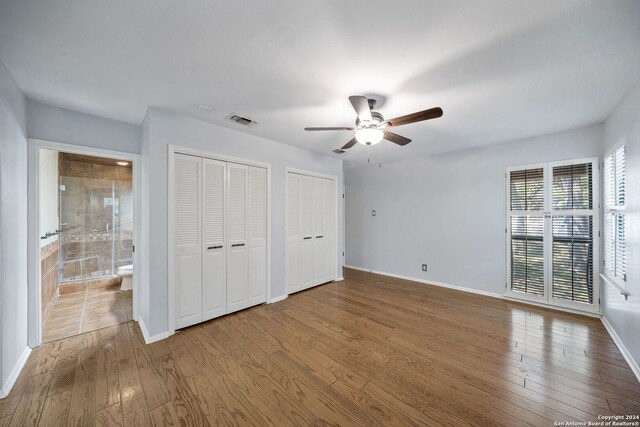 unfurnished bedroom featuring wood-type flooring, two closets, connected bathroom, and ceiling fan