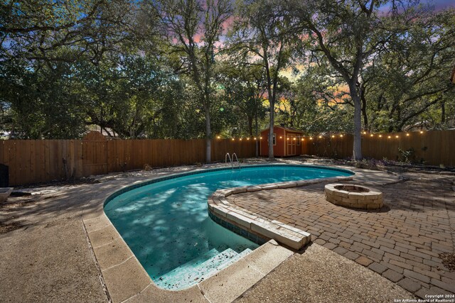 pool at dusk with a patio, a shed, and an outdoor fire pit