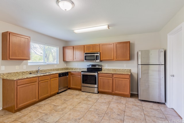 kitchen with appliances with stainless steel finishes, light stone countertops, and sink