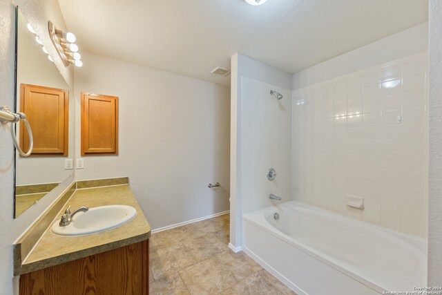 bathroom featuring a textured ceiling, tiled shower / bath combo, and vanity