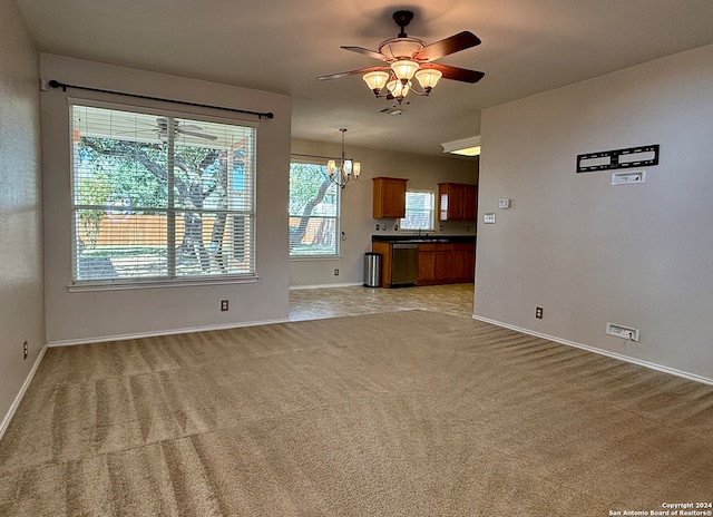 unfurnished living room with a healthy amount of sunlight, ceiling fan with notable chandelier, and light colored carpet