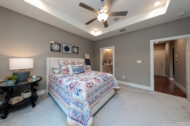 carpeted bedroom featuring a tray ceiling, ensuite bath, and ceiling fan