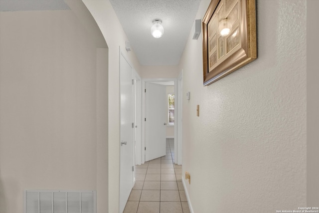 hall with a textured ceiling and light tile patterned flooring