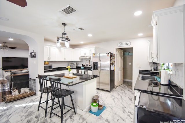 kitchen with ceiling fan, white cabinets, pendant lighting, stainless steel appliances, and a breakfast bar area