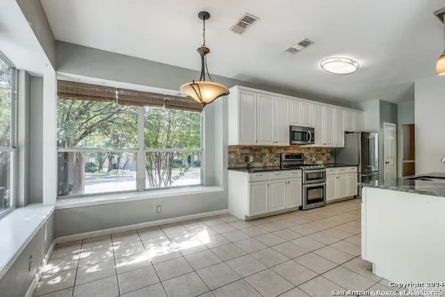 kitchen with appliances with stainless steel finishes, decorative backsplash, white cabinetry, light tile patterned floors, and pendant lighting