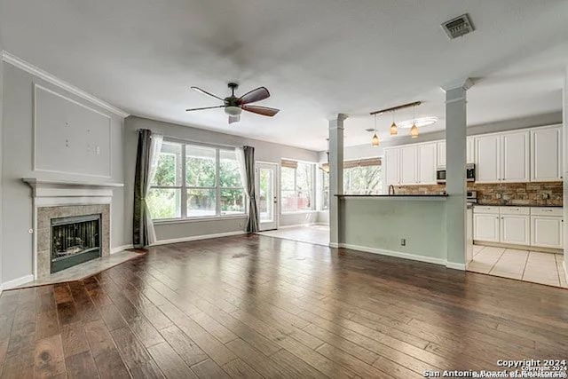 unfurnished living room featuring wood-type flooring, a tiled fireplace, ceiling fan, and ornate columns