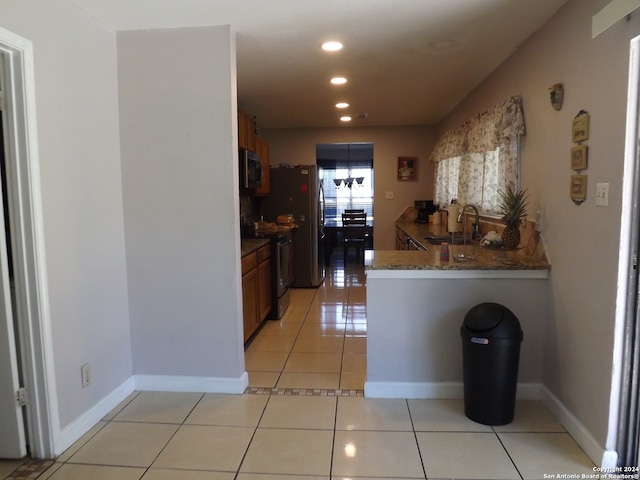 kitchen with appliances with stainless steel finishes, kitchen peninsula, light tile patterned floors, dark stone counters, and sink