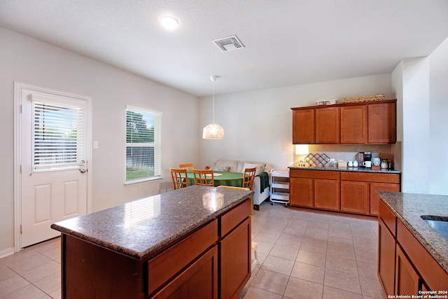 kitchen featuring light tile patterned floors, backsplash, dark stone countertops, decorative light fixtures, and a kitchen island