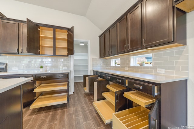 kitchen with dark brown cabinetry, vaulted ceiling, and backsplash