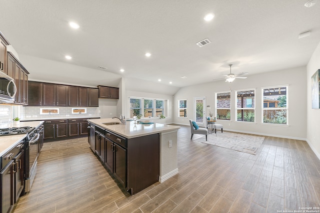 kitchen featuring tasteful backsplash, sink, a kitchen island with sink, dark brown cabinetry, and stainless steel appliances