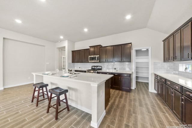 kitchen with appliances with stainless steel finishes, an island with sink, lofted ceiling, sink, and dark brown cabinetry