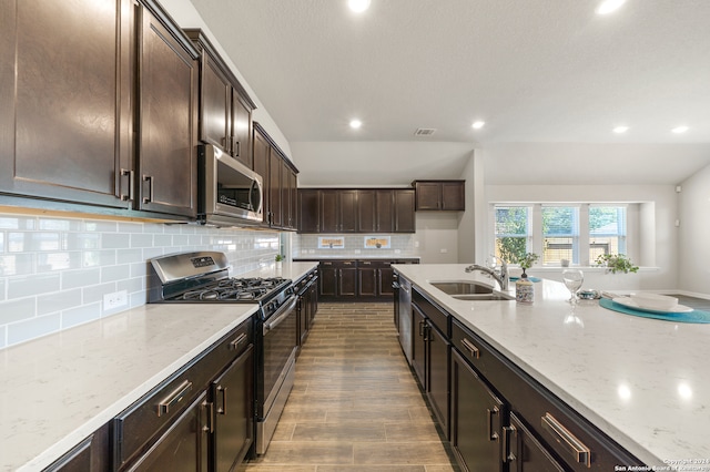 kitchen featuring appliances with stainless steel finishes, sink, backsplash, dark brown cabinetry, and light stone countertops