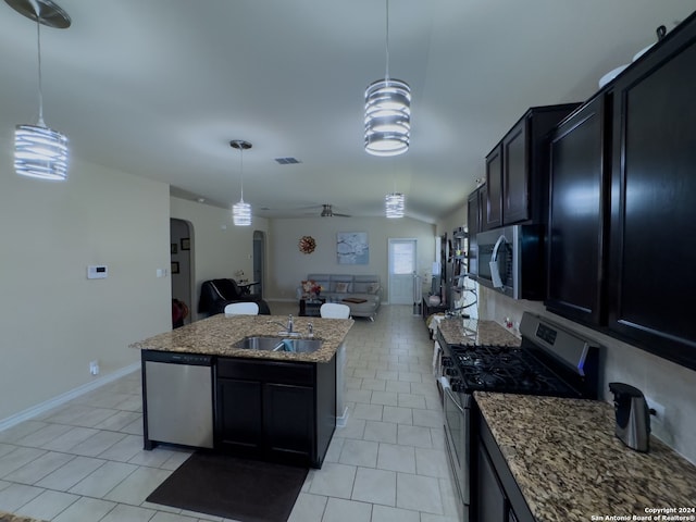 kitchen with sink, stainless steel appliances, a center island with sink, decorative light fixtures, and light stone countertops