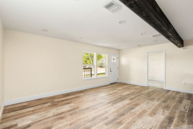 spare room featuring a textured ceiling, light hardwood / wood-style floors, and beam ceiling