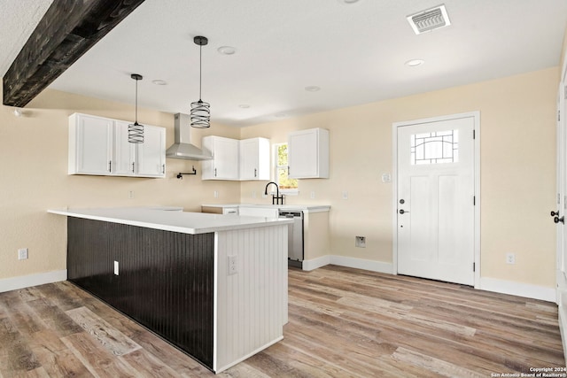 kitchen featuring beamed ceiling, stainless steel dishwasher, wall chimney range hood, white cabinetry, and light hardwood / wood-style floors