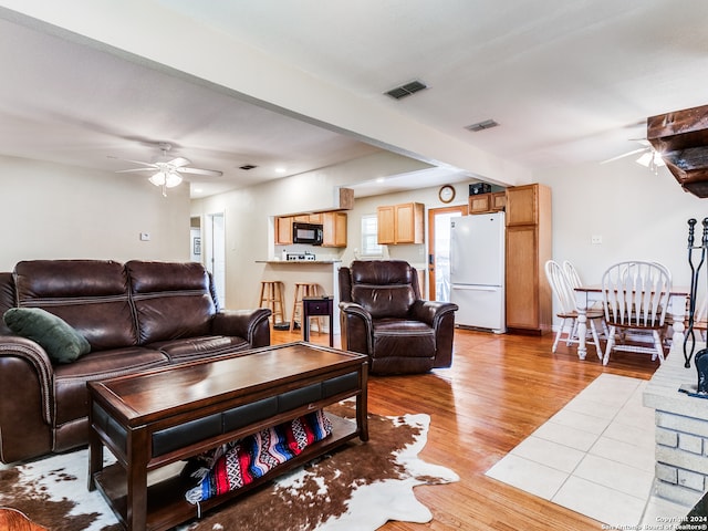 living room with light hardwood / wood-style floors, ceiling fan, and beamed ceiling