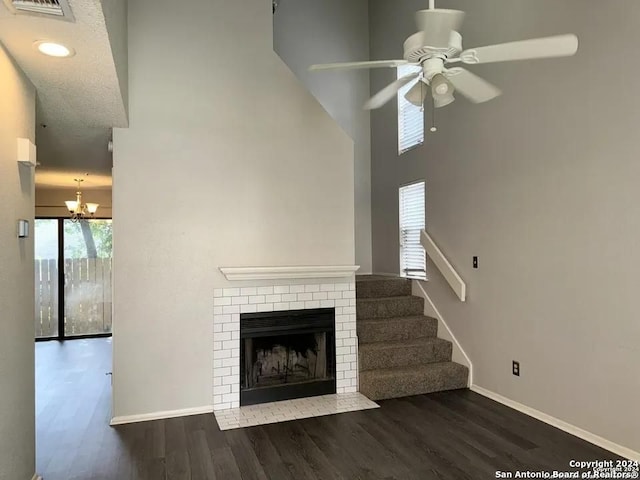 unfurnished living room with a brick fireplace, a high ceiling, ceiling fan, and dark hardwood / wood-style floors