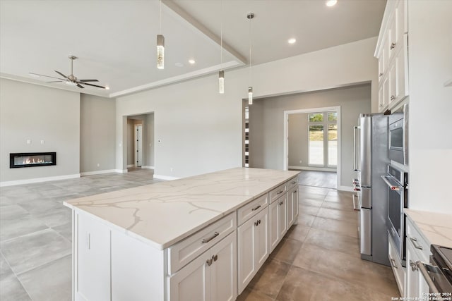 kitchen featuring light stone counters, white cabinets, ceiling fan, decorative light fixtures, and a center island