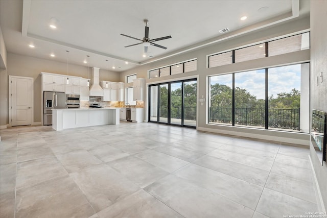 unfurnished living room with a high ceiling, ceiling fan, light tile patterned floors, and a raised ceiling