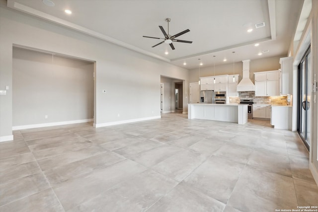 unfurnished living room featuring ceiling fan, light tile patterned floors, and a raised ceiling