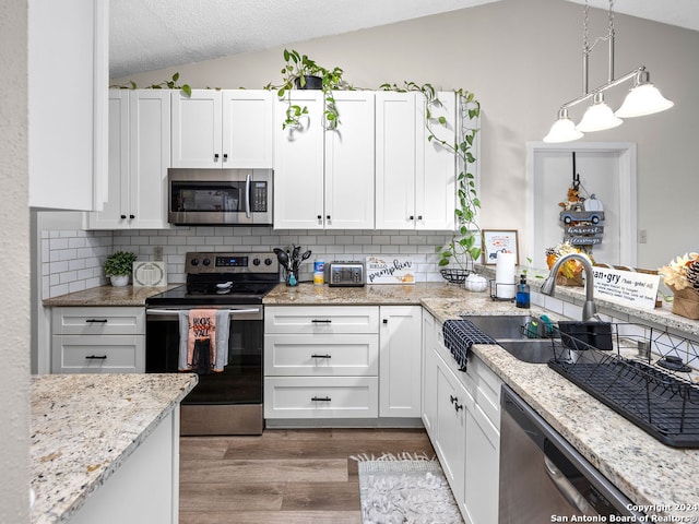 kitchen featuring hanging light fixtures, vaulted ceiling, white cabinets, stainless steel appliances, and sink