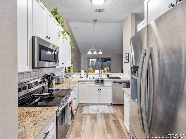 kitchen featuring white cabinets, hanging light fixtures, a textured ceiling, appliances with stainless steel finishes, and light wood-type flooring