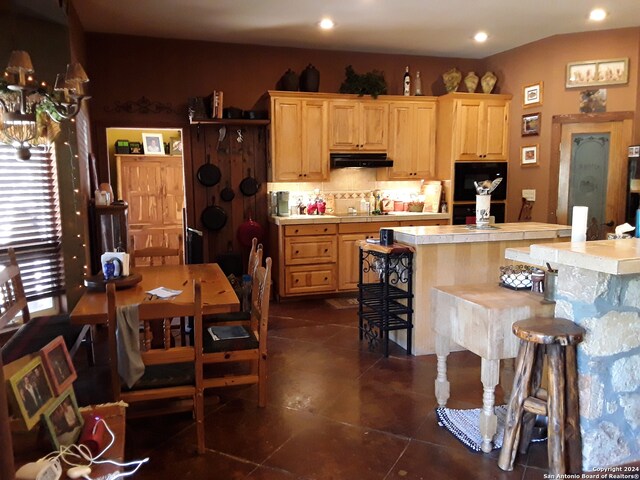 kitchen with a kitchen breakfast bar, a kitchen island, light brown cabinetry, and dark tile patterned flooring