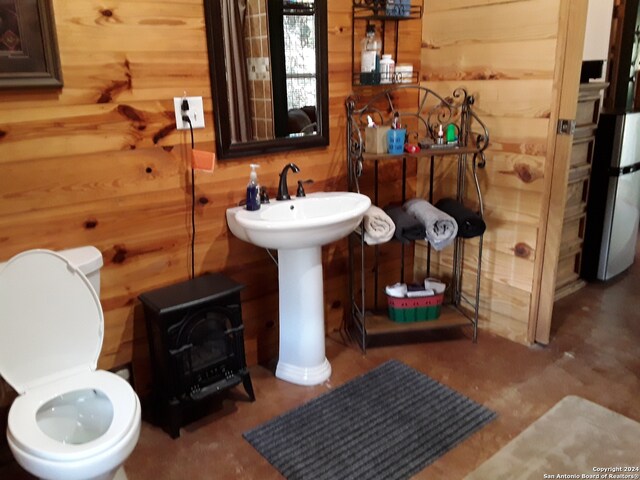 bathroom with wooden walls, toilet, and a wood stove